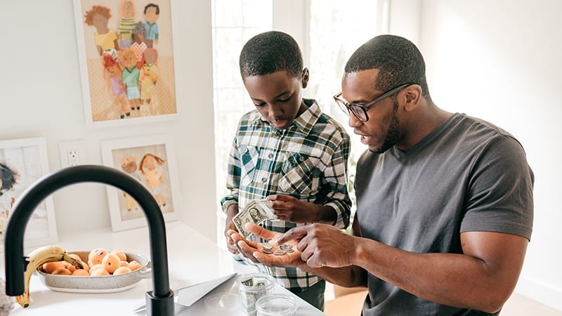 Black dad showing Black son how to count money teach kids about money