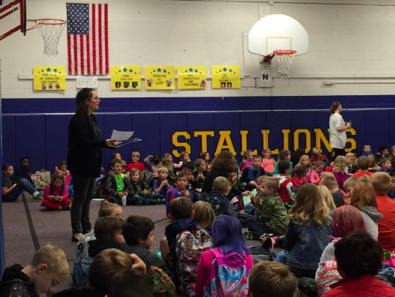 principal standing in front of a school assembly for principal's appreciation day idea