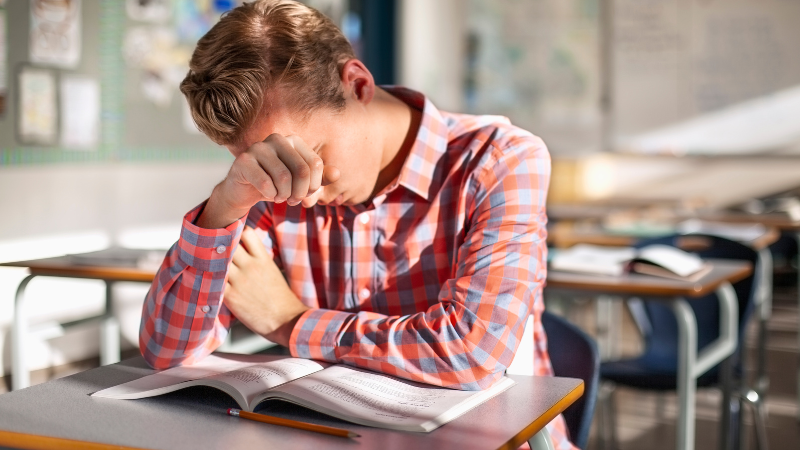 Teen covering face sitting at a classroom desk