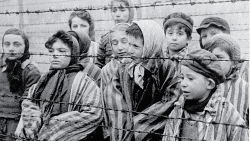 Photograph of children in a concentration camp behind a barbed-wire fence